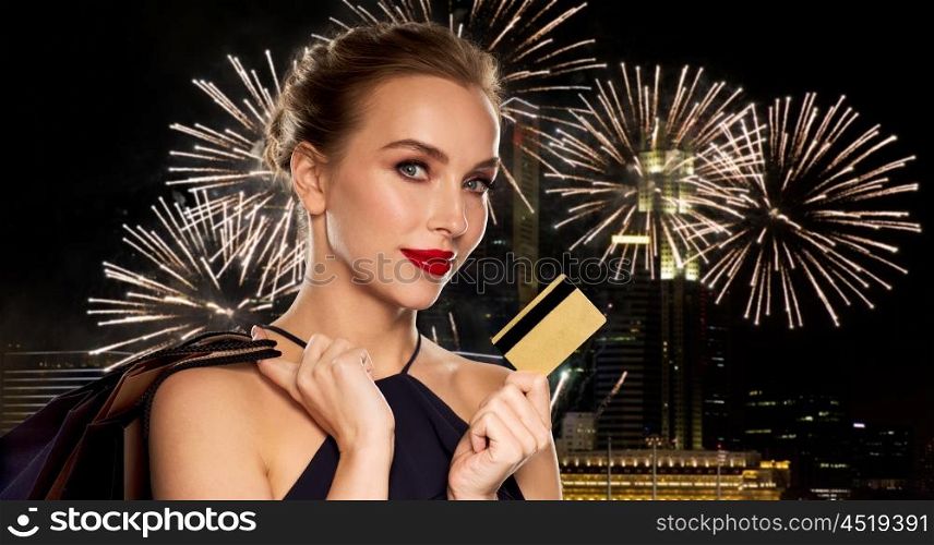 people, luxury and sale concept - beautiful woman with credit card and shopping bags over night singapore city and firework background