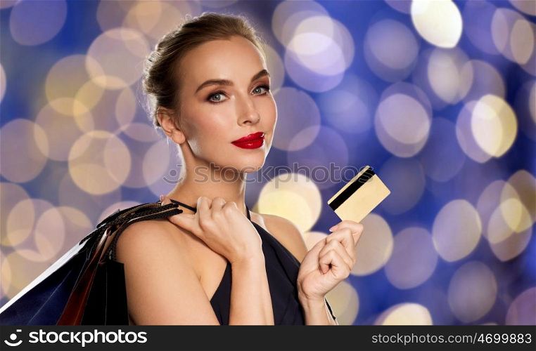 people, luxury and sale concept - beautiful woman with credit card and shopping bags over blue holidays lights background
