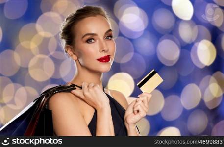 people, luxury and sale concept - beautiful woman with credit card and shopping bags over blue holidays lights background