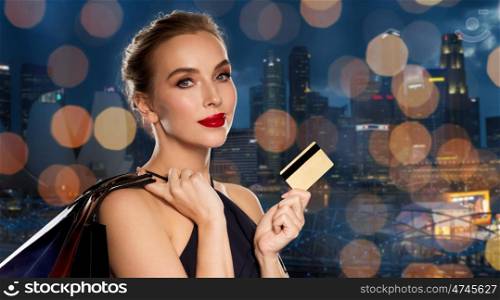 people, luxury and sale concept - beautiful woman with credit card and shopping bags over singapore city and holidays lights background