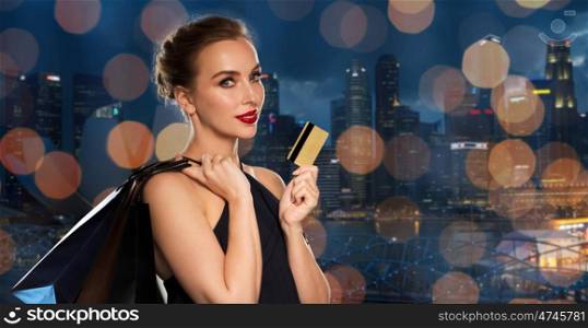 people, luxury and sale concept - beautiful woman with credit card and shopping bags over night singapore city skyscrapers and lights background