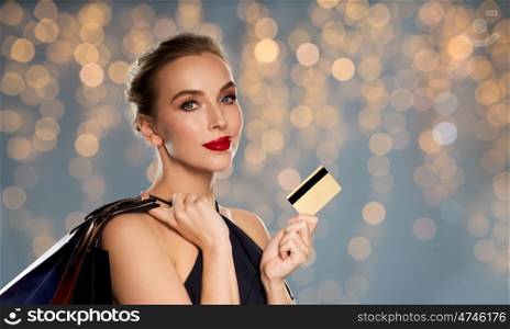 people, luxury and sale concept - beautiful woman with credit card and shopping bags over holidays lights background