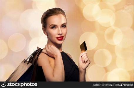 people, luxury and sale concept - beautiful woman with credit card and shopping bags over beige holidays lights background