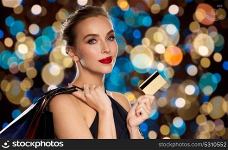 people, luxury and sale concept - beautiful woman with credit card and shopping bags over holidays lights background. woman with credit card and shopping bags
