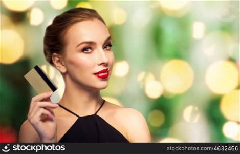 people, luxury, christmas, finances and shopping concept - beautiful woman with credit card over holidays lights background