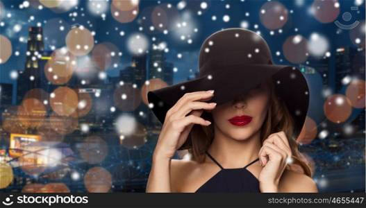 people, luxury, christmas, holidays and fashion concept - beautiful woman in black hat over night singapore city lights background and snow
