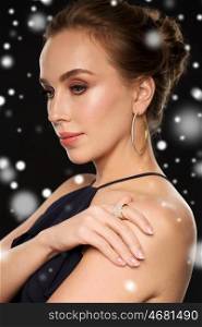people, luxury, christmas, holidays and jewelry concept - beautiful woman wearing diamond earring and ring over black background and snow