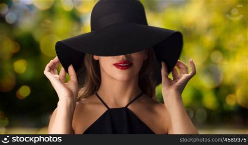 people, luxury, holidays and fashion concept - beautiful woman in black hat over green lights background