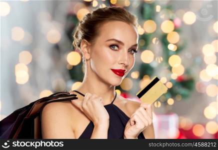 people, luxury, holidays and sale concept - beautiful woman with credit card and shopping bags over christmas tree lights background