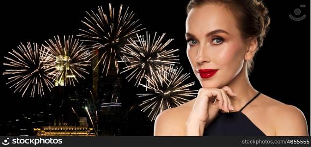 people, luxury, holidays, new year and fashion concept - beautiful woman in black with red lips over night city firework lights background