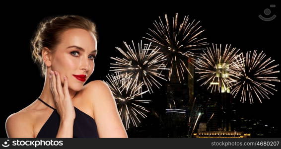 people, luxury, holidays, new year and fashion concept - beautiful woman in black with red lips over night city firework lights background