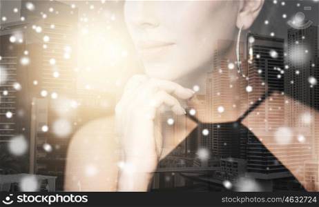 people, luxury, jewelry and christmas concept - beautiful woman in black wearing diamond earring and ring over dubai city background double exposure with highlight and snow