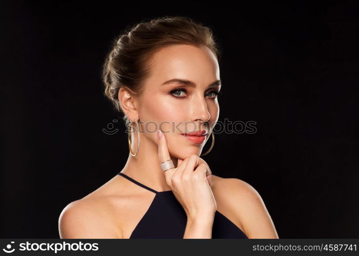 people, luxury, jewelry and fashion concept - beautiful woman in black wearing golden earrings and ring with diamonds over dark background