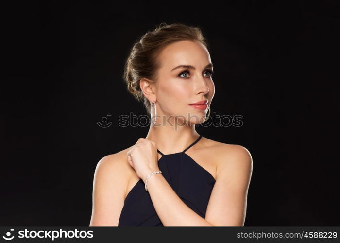 people, luxury, jewelry and fashion concept - beautiful woman in black wearing diamond earrings and bracelet over dark background