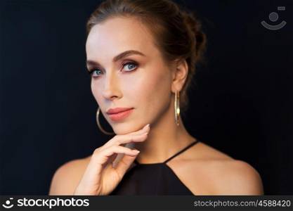 people, luxury, jewelry and fashion concept - beautiful woman in black wearing diamond earrings over dark background