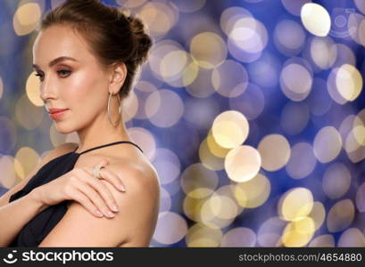 people, luxury, jewelry and fashion concept - beautiful woman in black wearing diamond earring and ring over blue holidays lights background