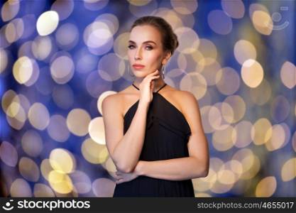people, luxury, jewelry and fashion concept - beautiful woman in black wearing diamond earrings over blue holidays lights background