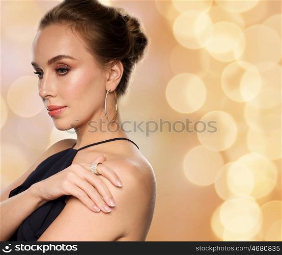 people, luxury, jewelry and fashion concept - beautiful woman in black wearing diamond earring and ring over beige holidays background