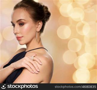 people, luxury, jewelry and fashion concept - beautiful woman in black wearing diamond earring and ring over beige holidays background