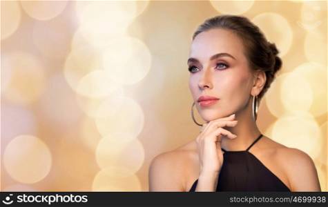 people, luxury, jewelry and fashion concept - beautiful woman in black wearing diamond earring and ring over holidays lights background
