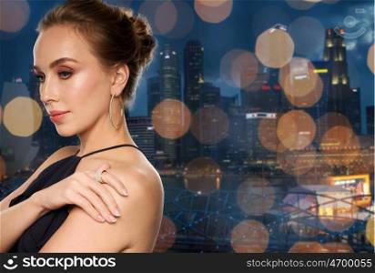 people, luxury, jewelry and fashion concept - beautiful woman in black wearing diamond earring and ring over night singapore city skyscrapers and lights background