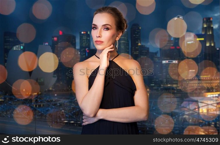 people, luxury, jewelry and fashion concept - beautiful woman in black wearing diamond earrings over night singapore city skyscrapers and lights background
