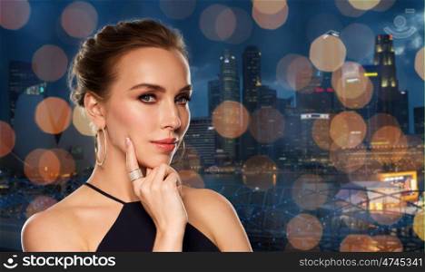 people, luxury, jewelry and fashion concept - beautiful woman in black wearing golden earrings and ring with diamonds over singapore city and holidays lights background