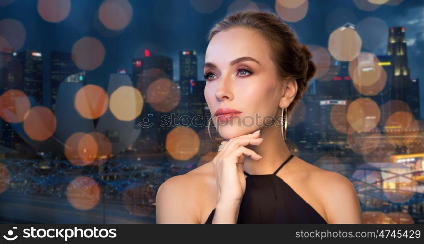 people, luxury, jewelry and fashion concept - beautiful woman in black wearing diamond earring and ring over singapore city and holidays lights background