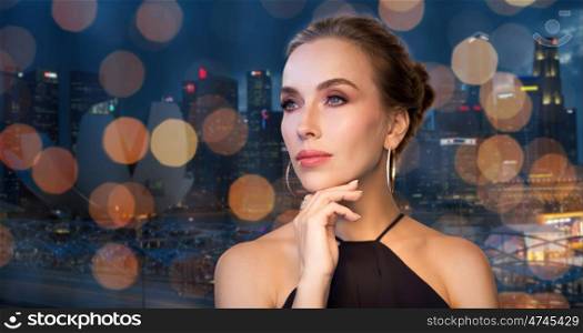 people, luxury, jewelry and fashion concept - beautiful woman in black wearing diamond earring and ring over singapore city and holidays lights background