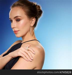 people, luxury, jewelry and fashion concept - beautiful woman in black wearing diamond earring and ring over blue background