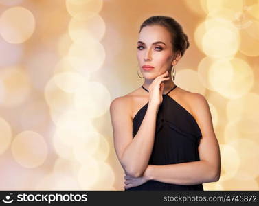 people, luxury, jewelry and fashion concept - beautiful woman in black wearing diamond earrings over beige holidays lights background