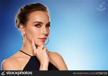 people, luxury, jewelry and fashion concept - beautiful woman in black wearing golden earrings and ring with diamonds over blue background