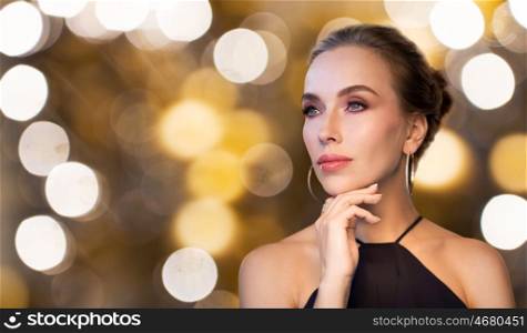 people, luxury, jewelry and holidays concept - beautiful woman in black wearing diamond earring and ring over lights background
