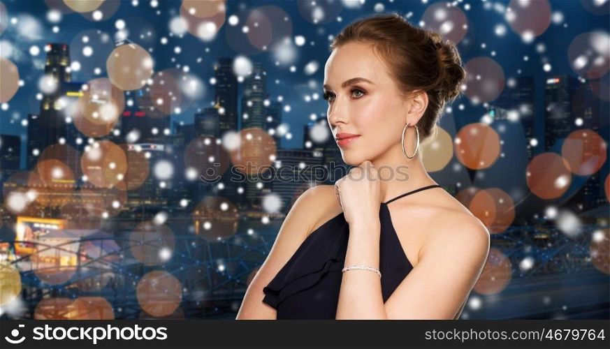 people, luxury, jewelry, christmas and holidays concept - beautiful woman in black wearing diamond earrings and bracelet over night singapore city lights background and snow