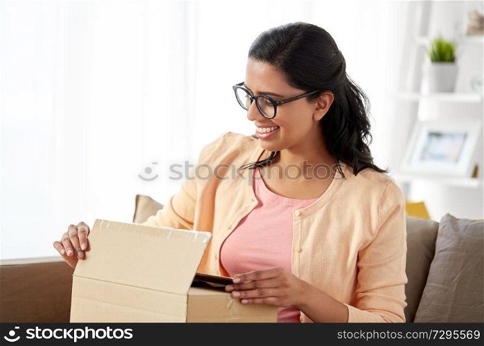 people, mail delivery and shipping concept - happy indian woman opening parcel box at home. happy indian woman opening parcel box at home
