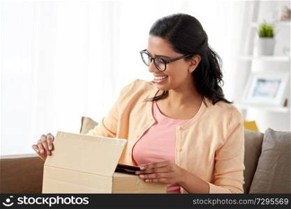 people, mail delivery and shipping concept - happy indian woman opening parcel box at home. happy indian woman opening parcel box at home