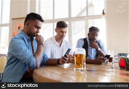 people, male friendship and technology concept - friends with smartphone drinking beer at bar or pub. male friends with smartphone drinking beer at bar