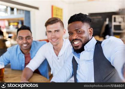 people, male friendship and technology concept - happy friends drinking beer and taking selfie at bar or pub. friends taking selfie and drinking beer at bar