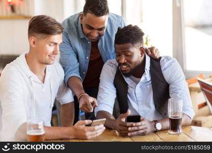 people, male friendship and technology concept - happy friends with smartphone drinking beer at bar or pub. male friends with smartphone drinking beer at bar