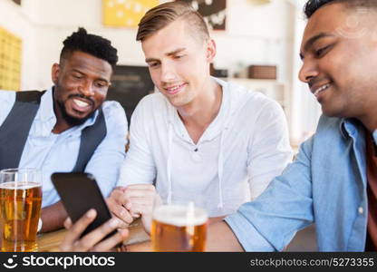 people, male friendship and technology concept - happy friends with smartphone drinking beer at bar or pub. male friends with smartphone drinking beer at bar