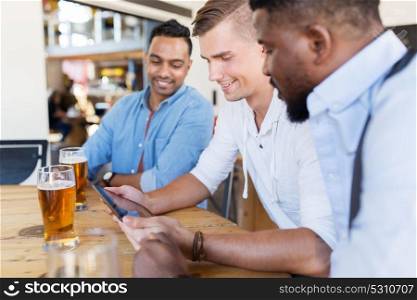 people, male friendship and technology concept - happy friends with tablet pc computer drinking beer at bar or pub. male friends with tablet pc drinking beer at bar