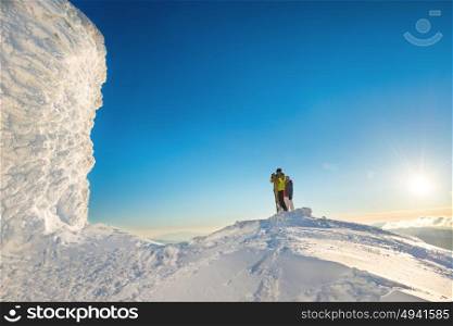 People man and woman on the top of the winter mountain in snow at sunset