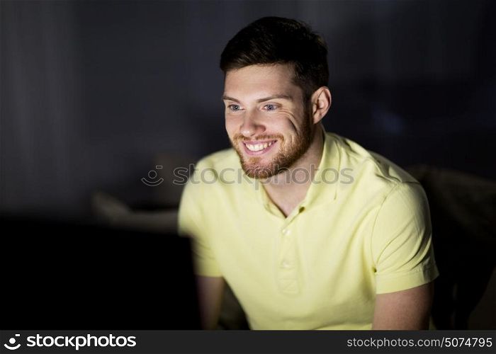 people, mass media, television and entertainment concept - happy smiling young man watching tv at night at home. happy smiling young man watching tv at night