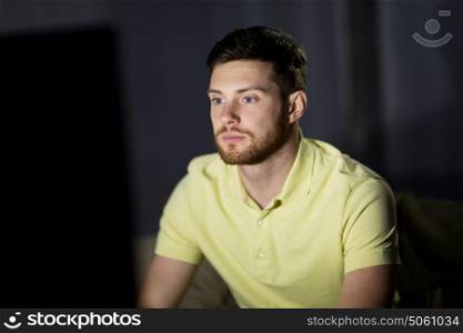 people, mass media, television and entertainment concept - young man watching tv at night at home. young man watching tv at night