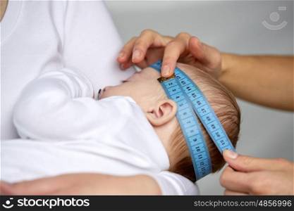 people, medical exam, healthcare and child care concept - close up of hands with tape measuring baby head