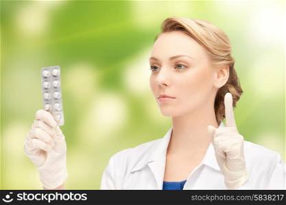 people, medication and warning gesture concept - young female doctor with pills pointing finger up over green background