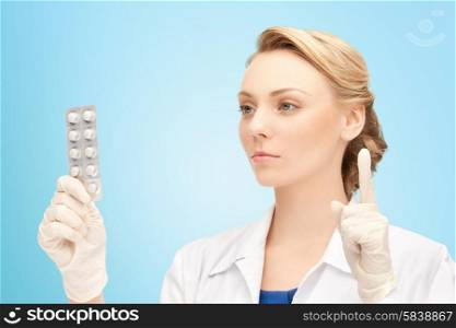 people, medication and warning gesture concept - young female doctor with pills pointing finger up over blue background
