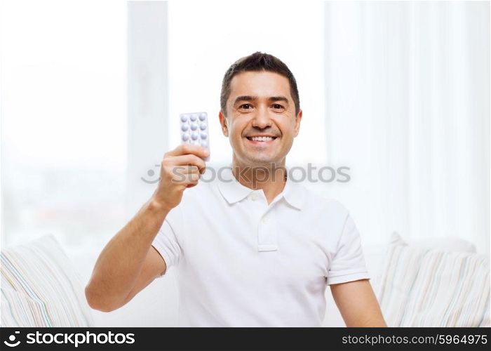 people, medication, medicine and health care concept - happy man showing pack of pills at home