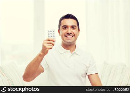 people, medication, medicine and health care concept - happy man showing pack of pills at home
