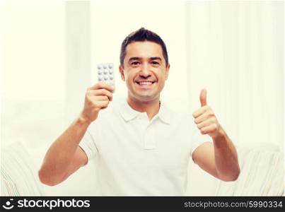 people, medication, medicine and health care concept - happy man showing thumbs up and holding pack of pills at home